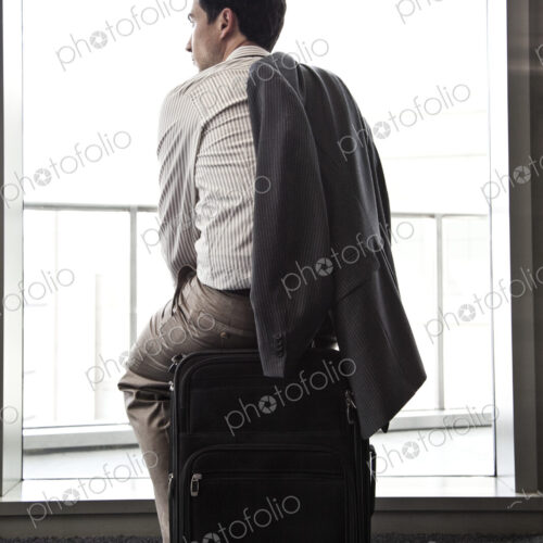 Businessman sitting on his luggage waiting for an airplane.