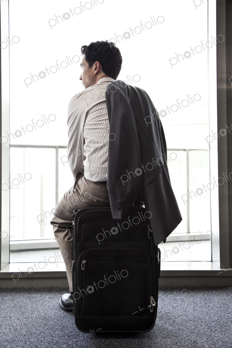Businessman sitting on his luggage waiting for an airplane.