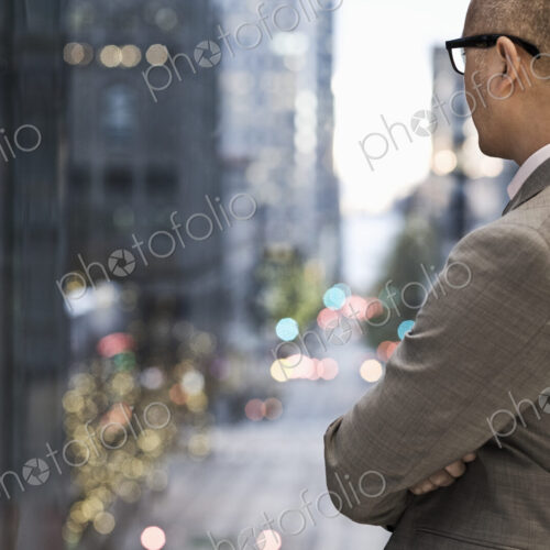 Businessman standing at a window looking out at a city view at dusk. Businessman standing at a window looking out at a city view at dusk.