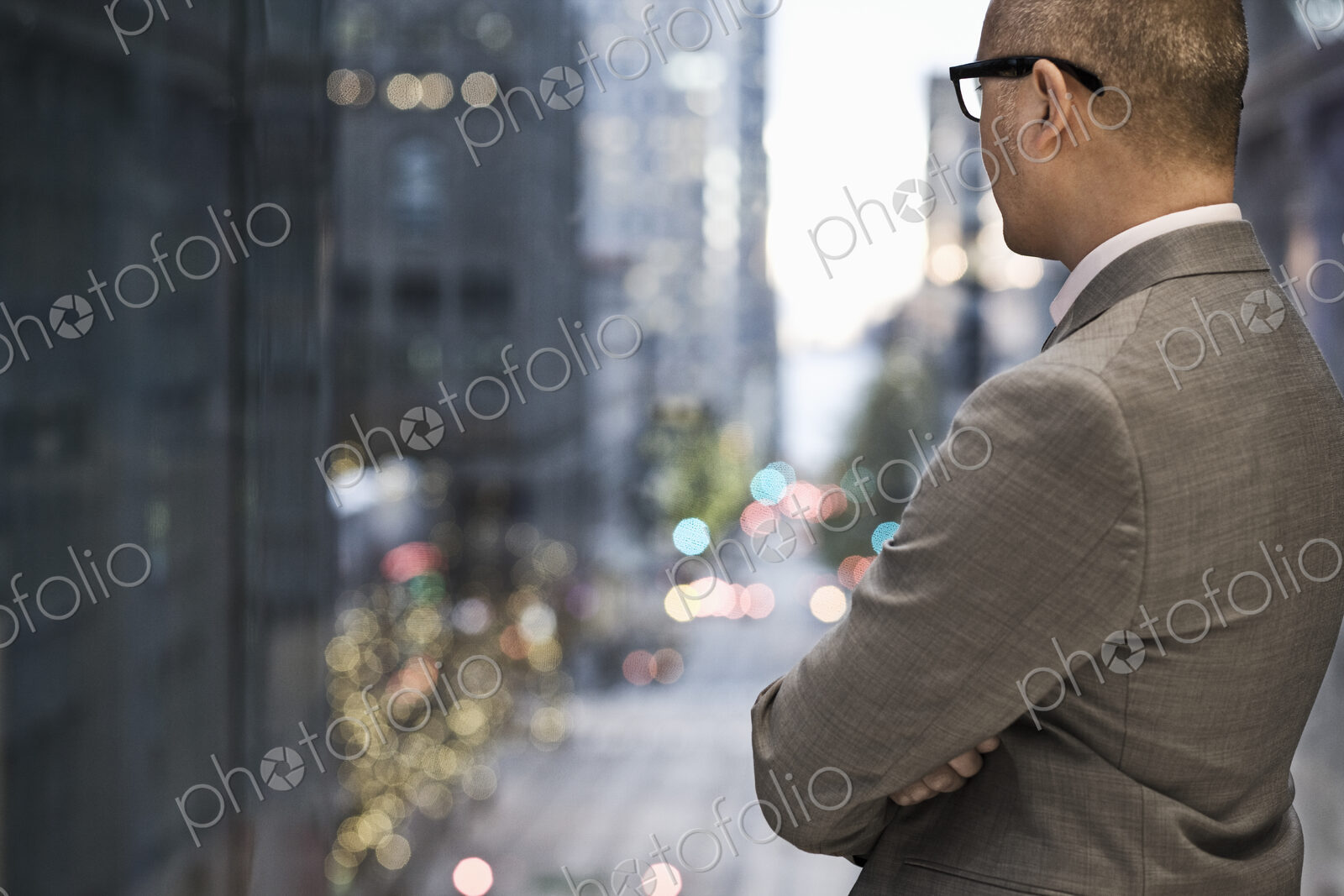 Businessman standing at a window looking out at a city view at dusk.