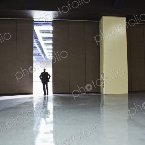 Businessman standing in a doorway between rooms in a convention center arena. Businessman standing in a doorway between rooms in a convention center arena.