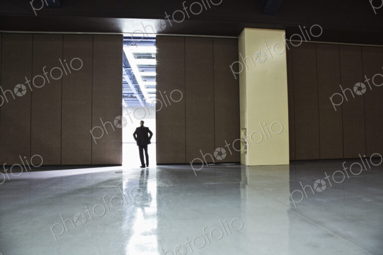Businessman standing in a doorway between rooms in a convention center arena.