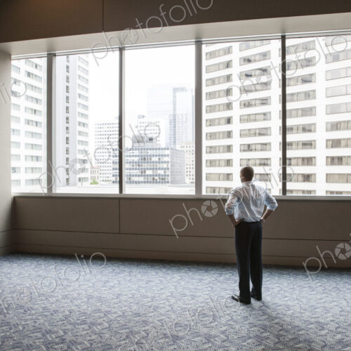 Businessman standing in empty space looking out a window at tall buildings