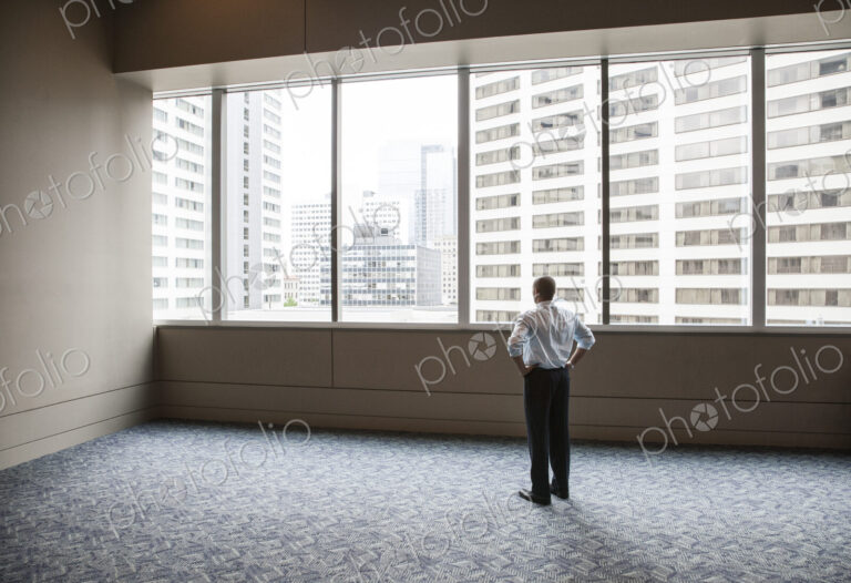 Businessman standing in empty space looking out a window at tall buildings