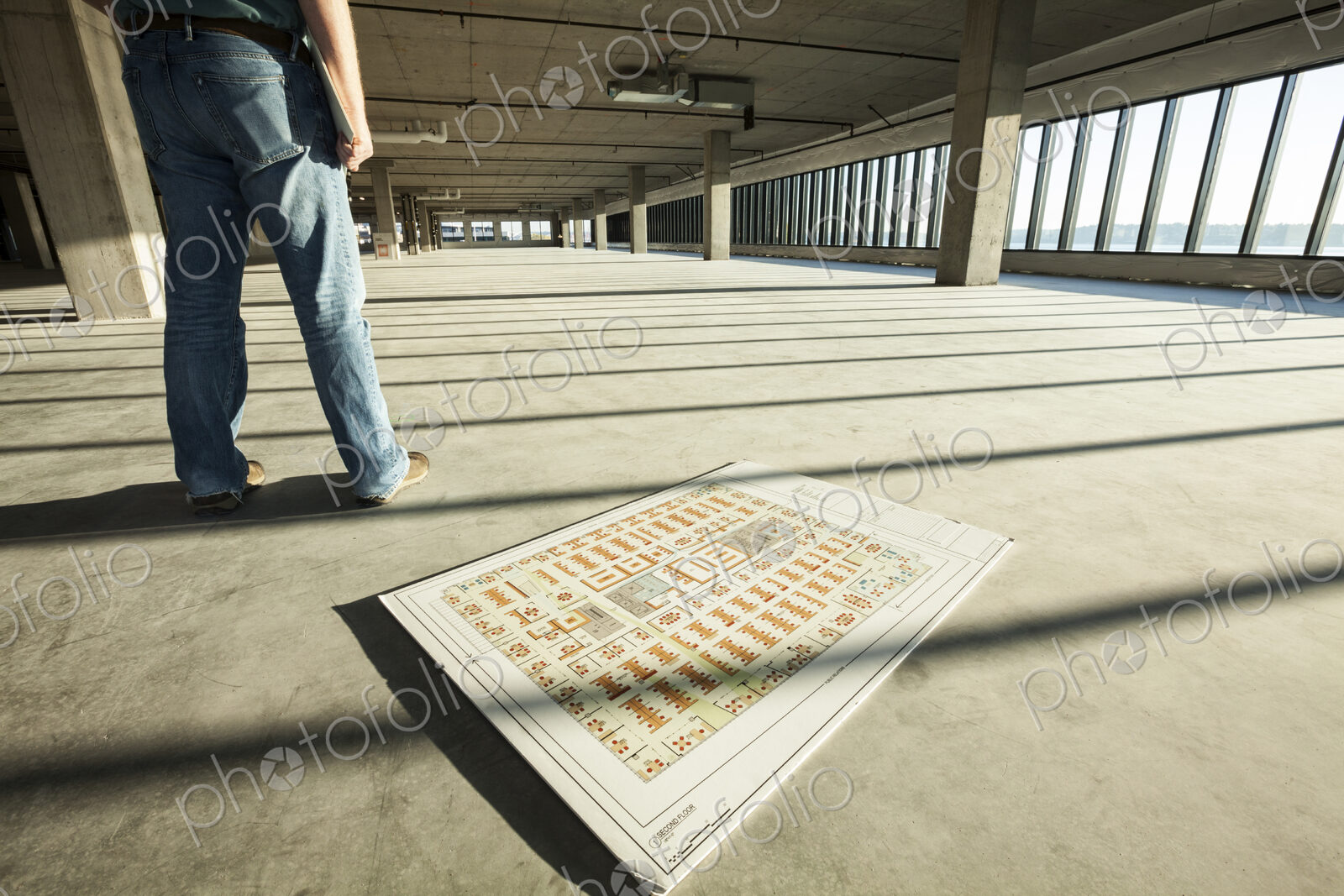 Businessman standing in the middle of an expanse of raw space, and architectural plans…