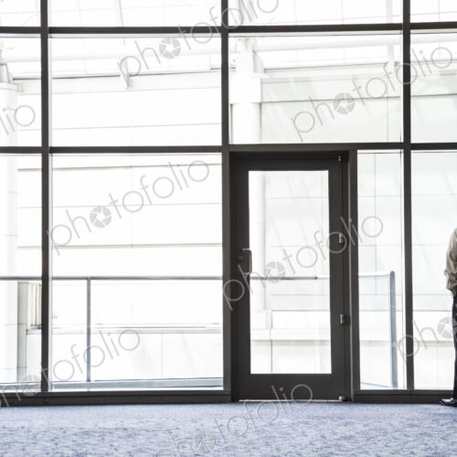 Businessman standing looking through a window in a large lobby area