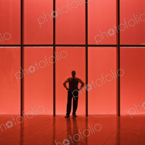 Businessman standing next to red tinted windows in an office lobby. Businessman standing next to red tinted windows in an office lobby.