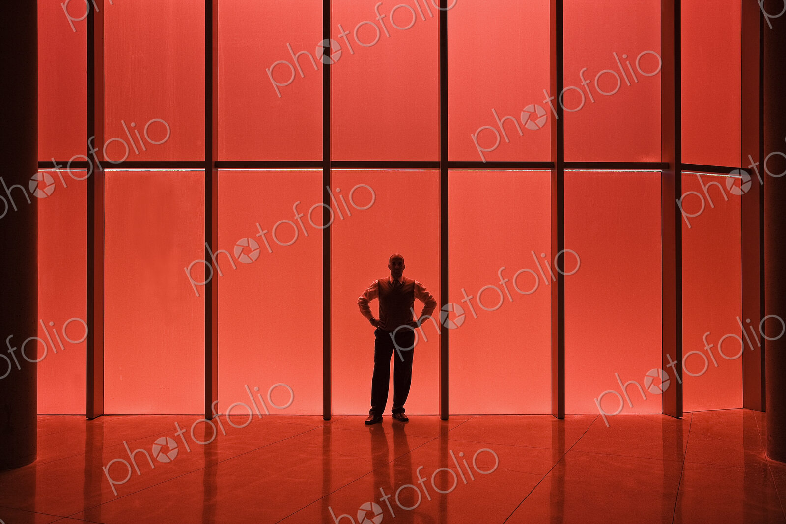 Businessman standing next to red tinted windows in an office lobby.