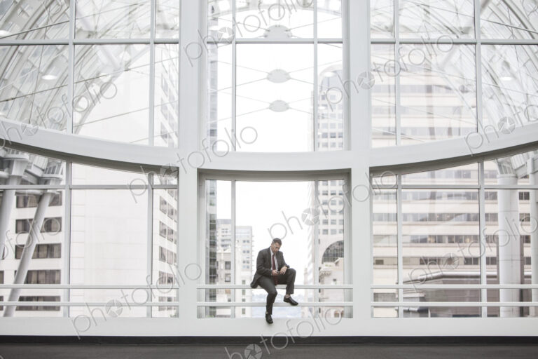 Businessman using his phone by a window in a convention center.