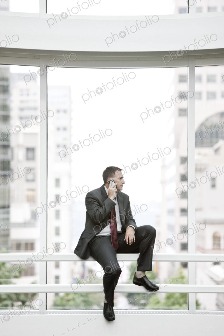 Businessman using his phone sitting on a railing