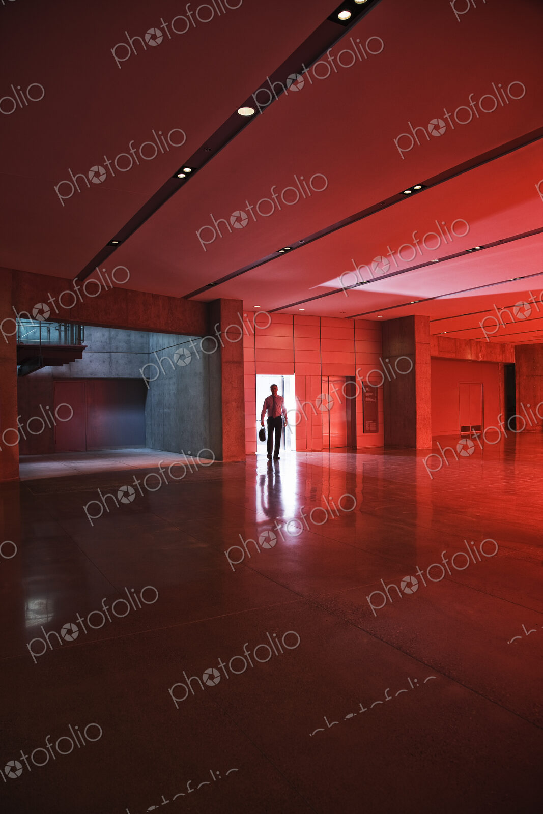 Businessman walks through the door of a lobby area that is lit by daylight through red…