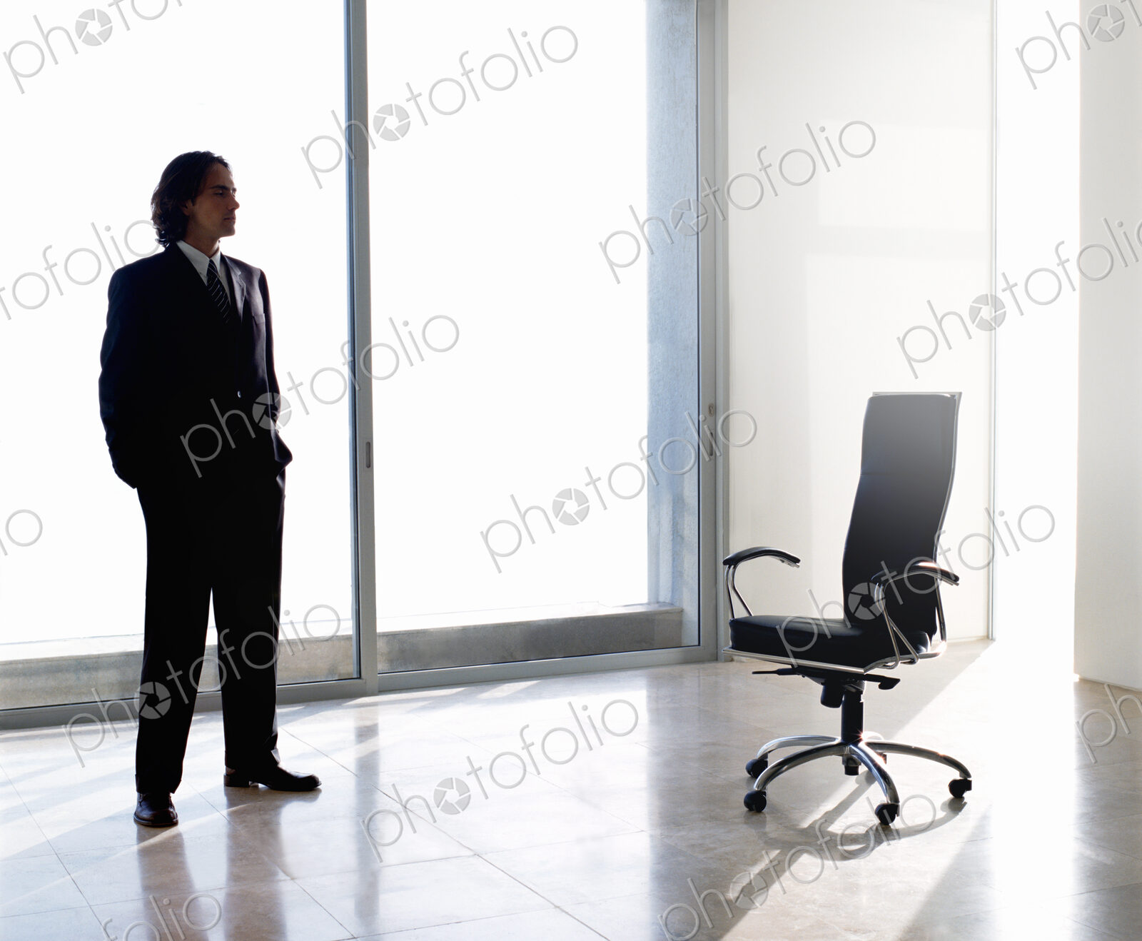 Businessman wearing dark suit standing indoors next to office chair in front of…