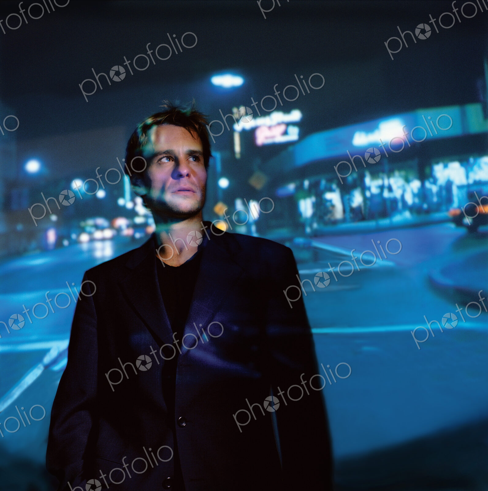 Businessman wearing suit standing at a street corner in a city at night, looking up.