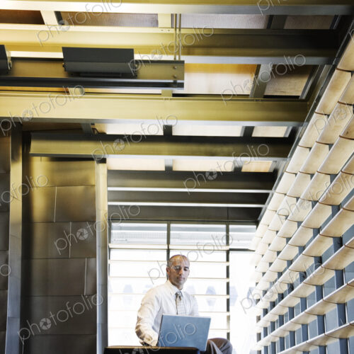 Businessman working on a laptop computer in the lobby of a large offfice building.