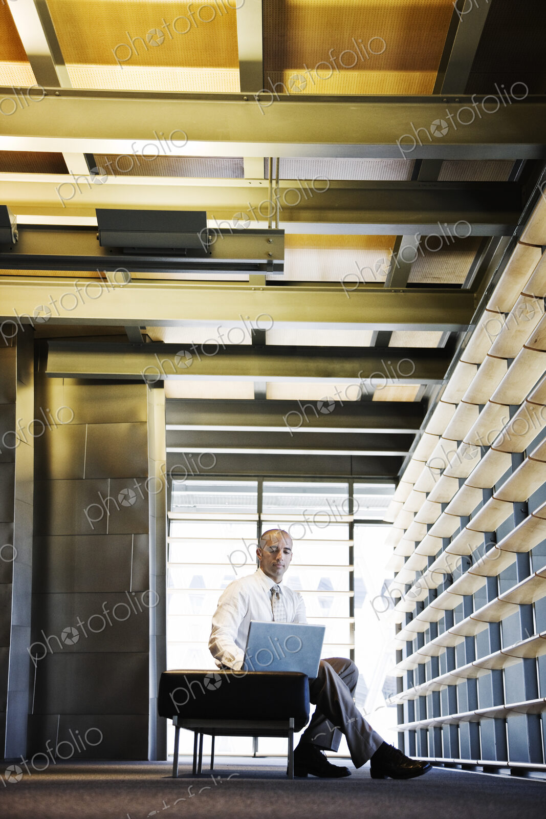 Businessman working on a laptop computer in the lobby of a large office building.