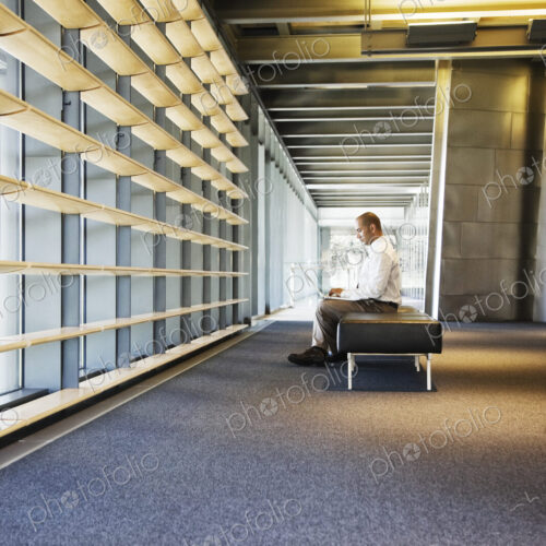 Businessman working on a laptop computer in the lobby of a large offfice building.