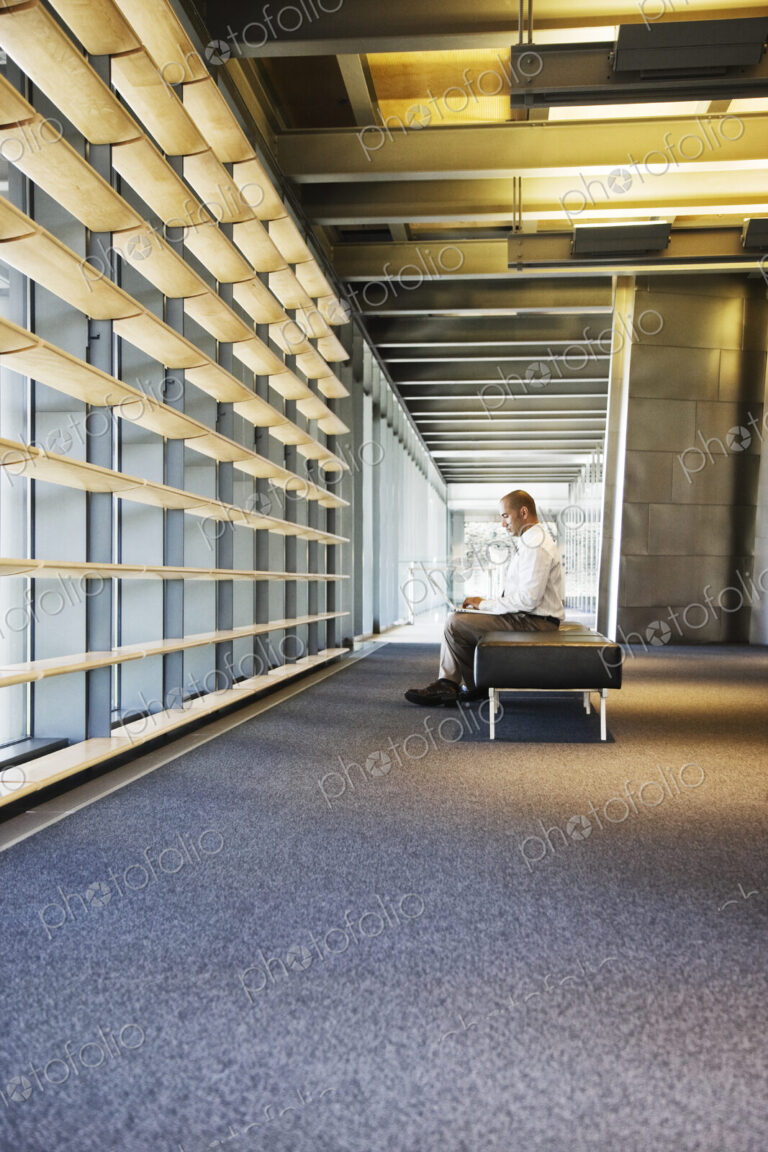 Businessman working on a laptop computer in the lobby of a large offfice building.