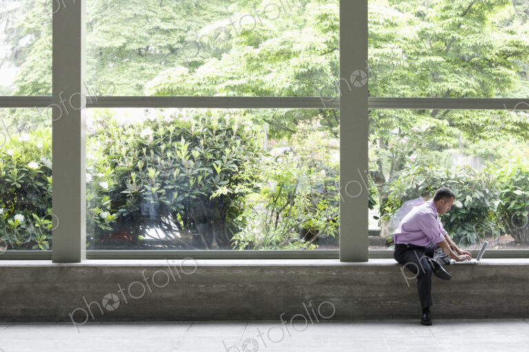 Businessman working on a notebook computer in front of a large window in a convention…