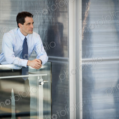 Businesssman standing at a railing in a conference centre lobby.