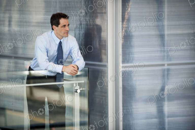 Businesssman standing at a railing in a conference centre lobby.