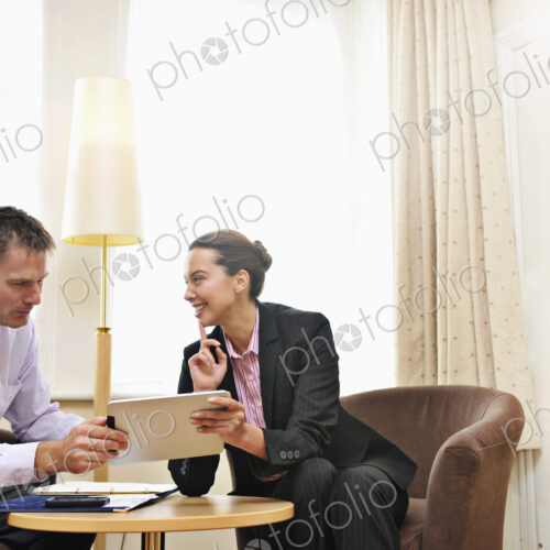 Businesswoman and man having meeting in hotel lobby or room, looking at ipad.