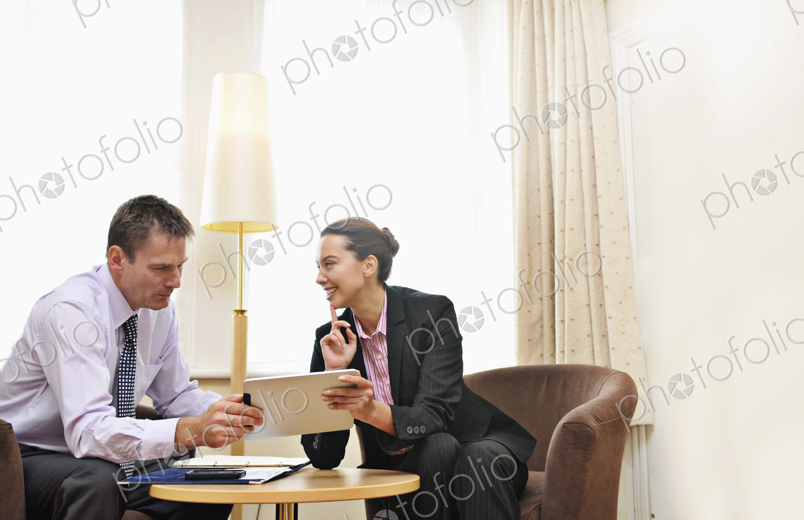 Businesswoman and man having meeting in hotel lobby or room, looking at ipad.