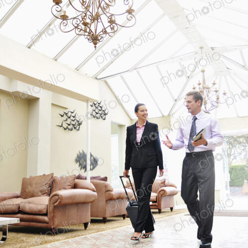 Businesswoman and man walking through hotel lobby, business travel.