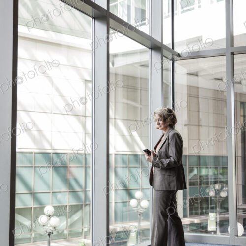 Businesswoman checking her cell phone for messages by a window