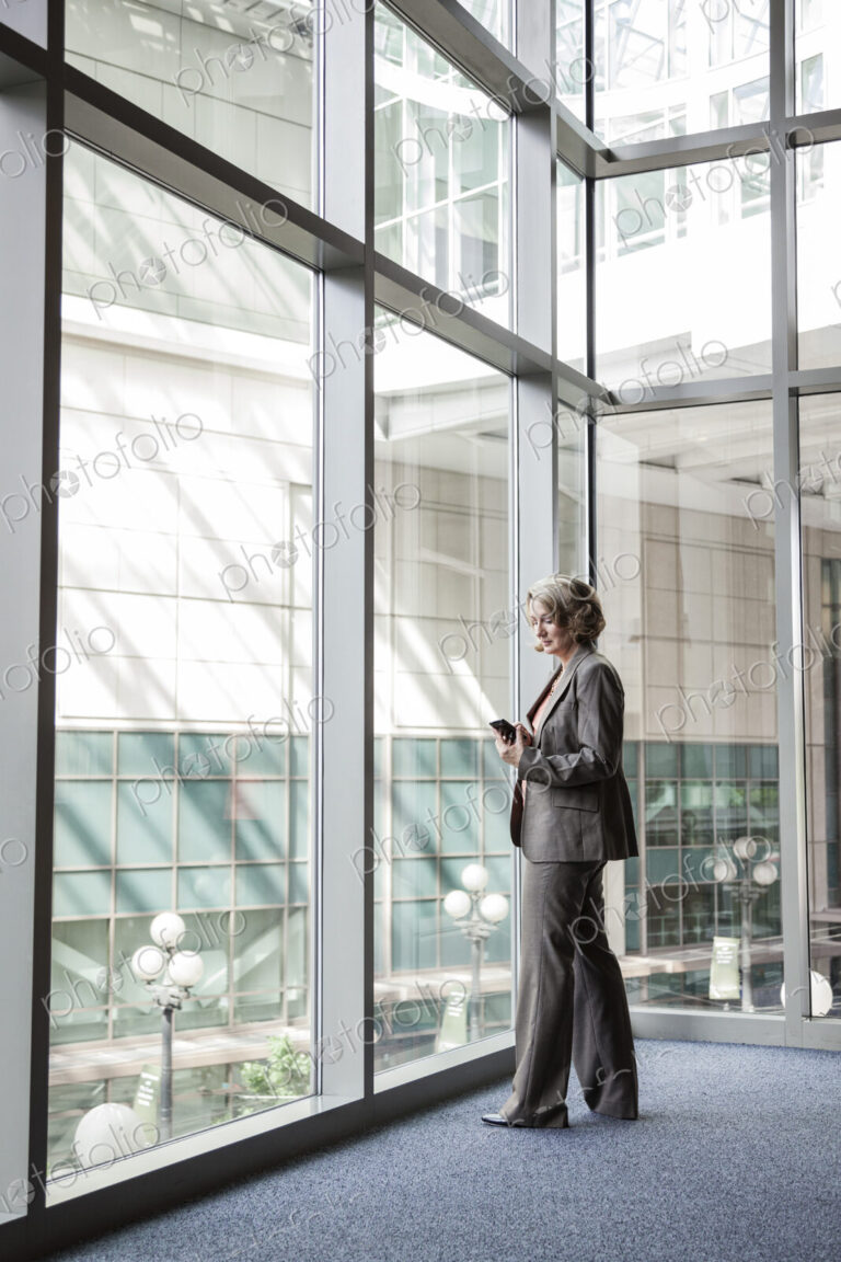Businesswoman checking her cell phone for messages by a window