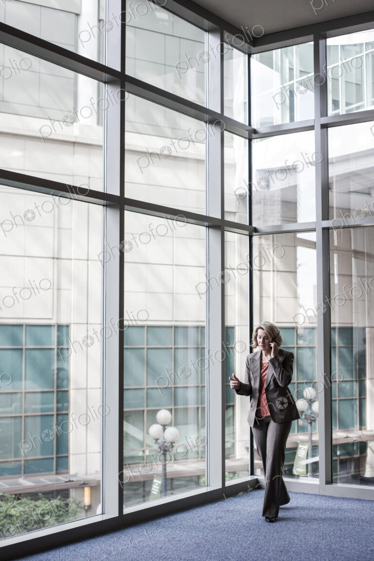 Businesswoman on a cell phone by large window in a convention center lobby.