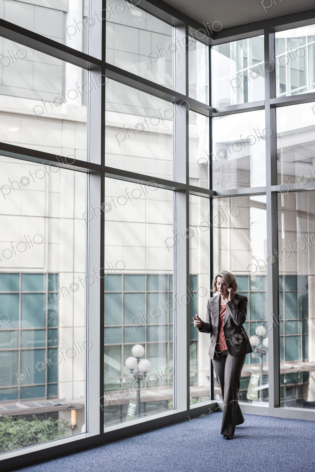 Businesswoman on a cell phone by large window in a convention center lobby.
