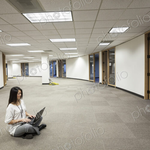 Businesswoman sitting working on a laptop computer in the middle of an empty office Businesswoman sitting working on a laptop computer in the middle of an empty office