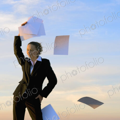 Businesswoman throwing paperwork into the wind with clear sky behind.