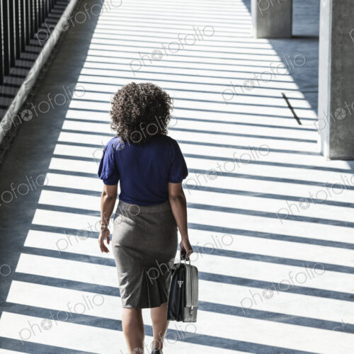 Businesswoman walking through large empty office space lit by the afternoon sun.