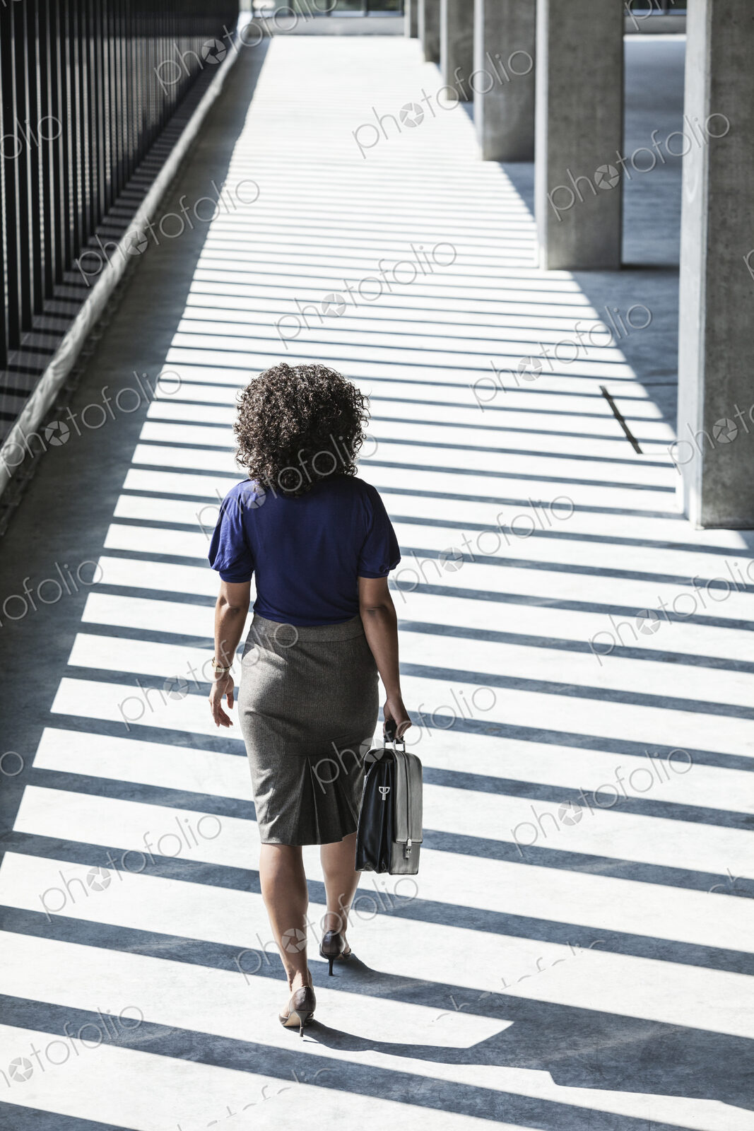 Businesswoman walking through large empty office space lit by the afternoon sun.