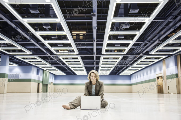 Businesswoman working on a laptop sitting on the floor of a convention center