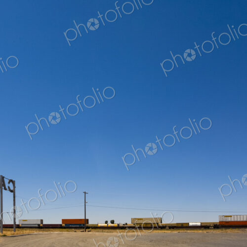 Cafe Sign, a tall sign by the railroad track, a freight train and box cars on the rails.
