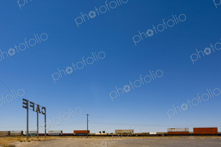 Cafe Sign, a tall sign by the railroad track, a freight train and box cars on the rails.