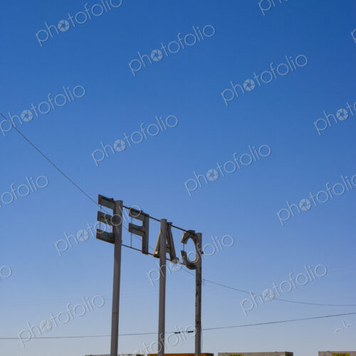 Cafe Sign, large letters on tall posts on flat land, above a railroad with containers. Cafe Sign, large letters on tall posts on flat land, above a railroad with containers.