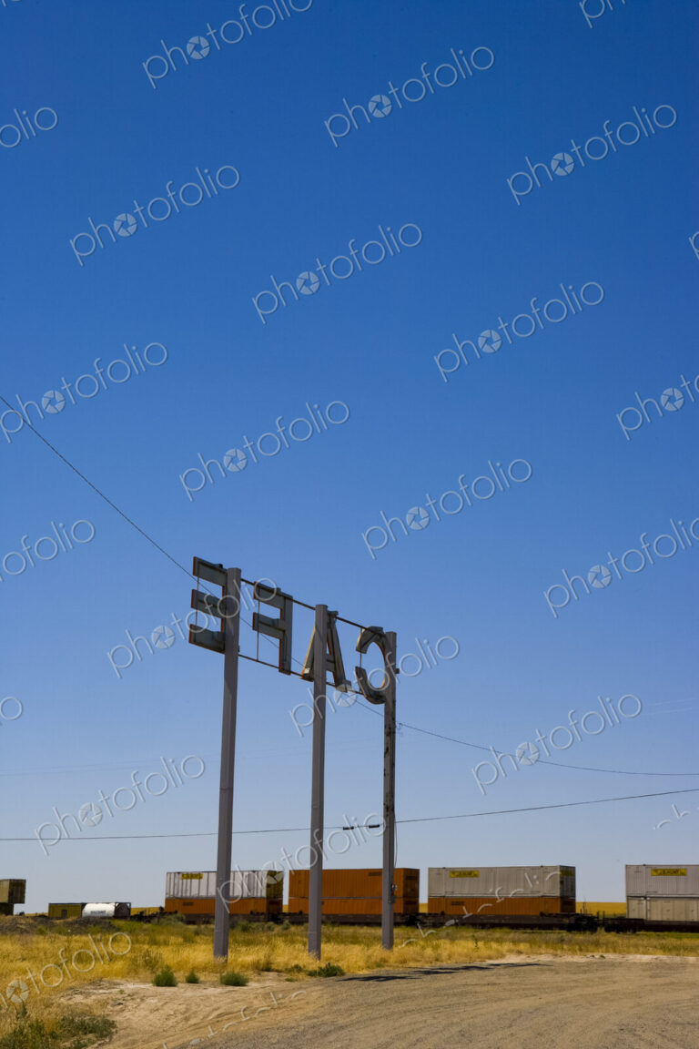 Cafe Sign, large letters on tall posts on flat land, above a railroad with containers.