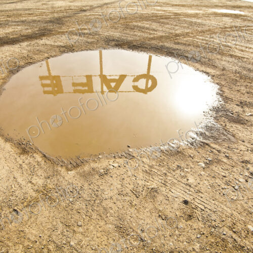 Cafe sign reflection in puddle of water on the ground in the dirt.