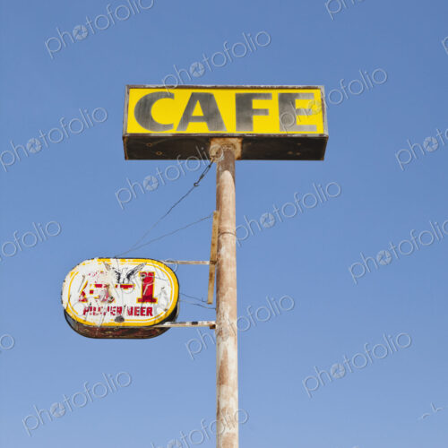 Cafe sign, rusted and faded, on a pole, blue sky background.