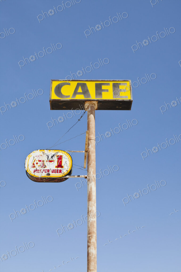 Cafe sign, rusted and faded, on a pole, blue sky background.