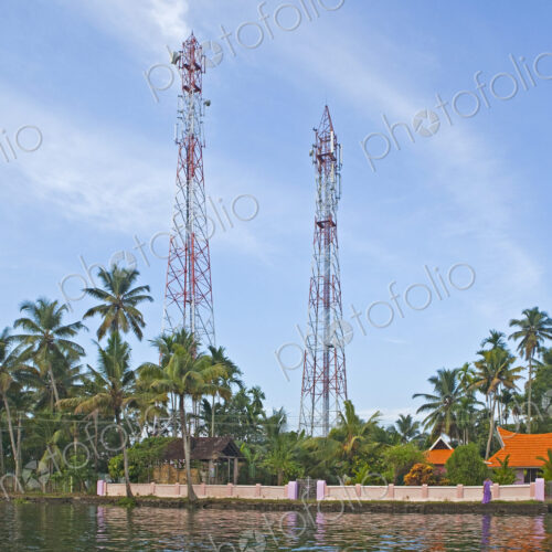 Calm backwaters in Kerala outside Alleppey, houses and tall radio masts among palm…