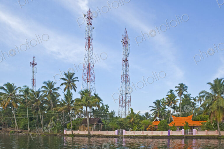 Calm backwaters in Kerala outside Alleppey, houses and tall radio masts among palm…