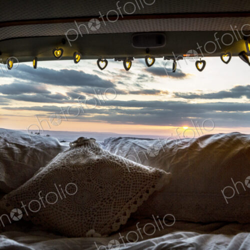 Camper van with cushion and fairy lights, view through rear window at sunset. Camper van with cushion and fairy lights, view through rear window at sunset.