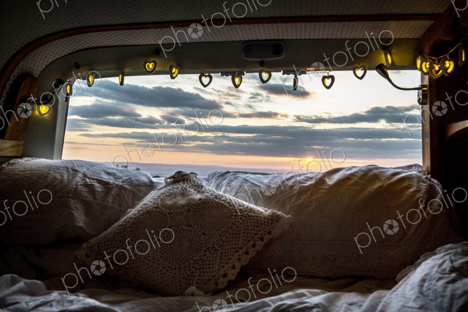 Camper van with cushion and fairy lights, view through rear window at sunset.