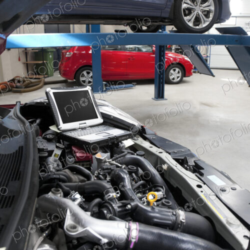 Car in a workshop and a computer running diagnostics on the engine.