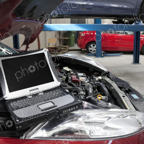 Car in a workshop and a computer running diagnostics on the engine.