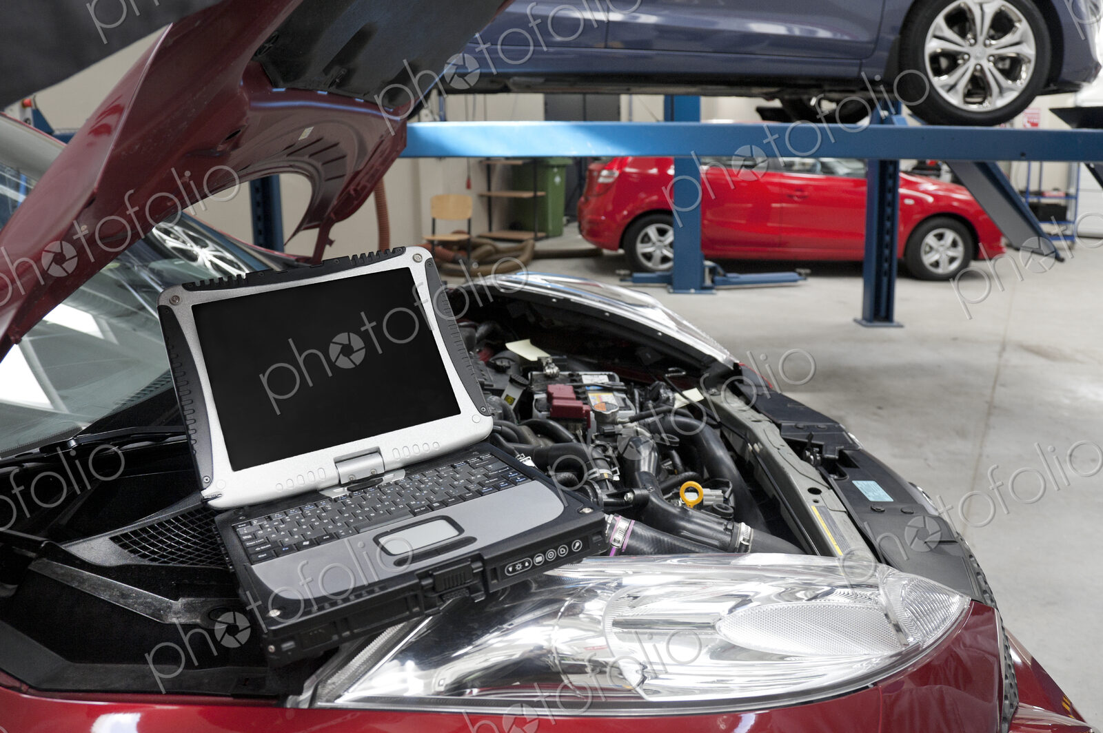 Car in a workshop and a computer running diagnostics on the engine.